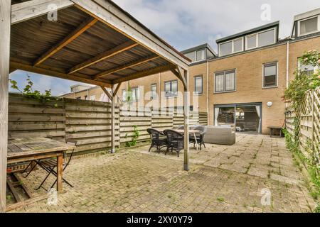 Ein großer Blick auf einen gemütlichen Hinterhof mit einer Pergola, Gartenmöbeln, Pflastersteinen und einem Wohngebäude im Hintergrund. Stockfoto