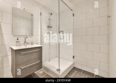 Modernes Bad mit verglaster Dusche, weißen Wandfliesen und stilvollem Kosmetikbereich mit Waschbecken. Stockfoto