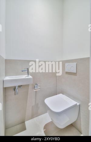 Ein modernes Badezimmer mit eleganter Toilette mit Wandaufhängung und minimalistischem Waschbecken mit modernem Chrom-Wasserhahn. Stockfoto