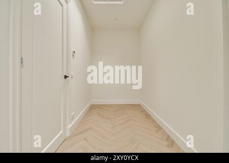 Ein sauberer, heller Innenkorridor mit weißen Wänden und stilvollem Holzfußboden mit Fischgrätenmuster. Stockfoto