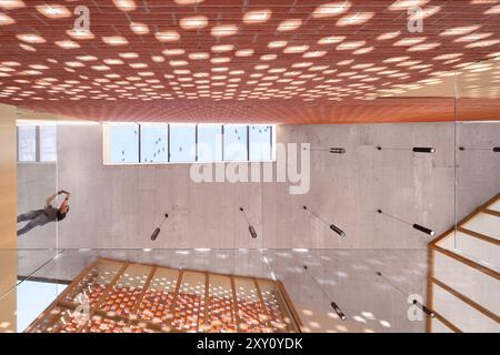 Dieses eindrucksvolle Auditorium verfügt über eine elegante Betonoberfläche und eine innovative Decke mit Ziegelmuster, die das Umgebungslicht durchfiltert, cr Stockfoto
