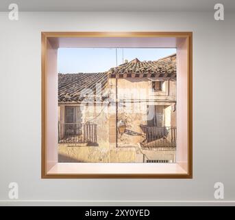 Ein modernes Fenster umrahmt einen malerischen Blick auf verwitterte, historische Gebäude unter klarem Himmel, die alte und neue architektonische Stile kontrastieren. Stockfoto
