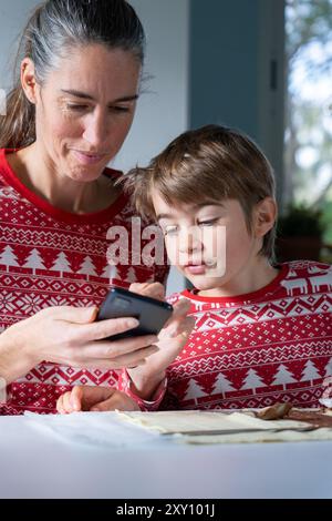 Mutter und Sohn suchen ein Rezept für ein Weihnachtsdessert auf dem Handy in Weihnachtskleidung Stockfoto