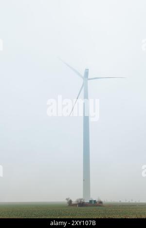 Eine Windturbinenmühle im Feld auf nebligem nebeligem, regnerischem Feld, schlechte Sicht am kalten Frühlingsherbstmorgen. Saisonales schlechtes Regenwetter Stockfoto