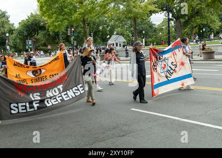 Washington DC, USA - 19.08.2024: Eine Gruppe von Menschen marschiert die Straße hinunter mit Schildern, auf denen steht: "Völkermord ist keine Selbstverteidigung." Stockfoto