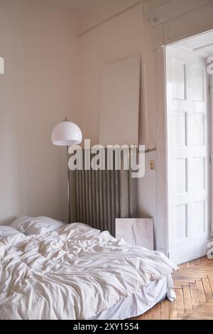 Ein helles und ruhiges Schlafzimmer mit weißem Bett, moderner Lampe und weichem Tageslicht. Einfache Einrichtung mit einem Hauch von Minimalismus und gemütlichem Komfort. Stockfoto