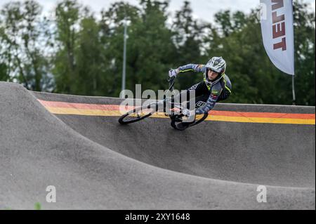 Tukums, Lettland - 10. August 2024: Ein Junge fährt mit seinem BMX-Fahrrad auf einer von Bäumen umgebenen Pumpstrecke. Stockfoto