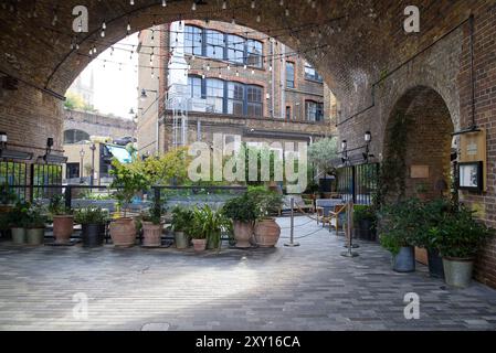 Restaurant und Cafe Stühle von Borough Yards unten Dirty Lane unter den Eisenbahnbögen. Tische und Stühle mit Blumen schmücken den Bereich. London Stockfoto