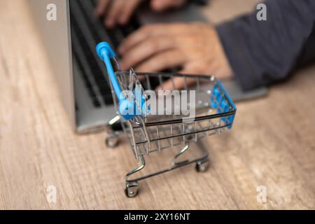 Nahaufnahme des Mini-Einkaufswagens und der Hände, die auf dem Laptop tippen. Online-Shopping-Konzept. Stockfoto