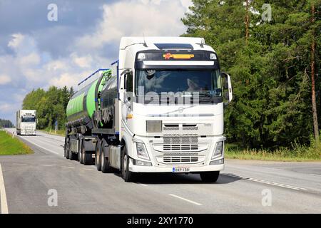 Zwei weiße Volvo FH-Lkws, ein Tankfahrzeug, ein LKW und ein Anhänger transportieren Güter auf der Autobahn 2 an einem Sommertag. Jokioinen, Finnland. August 2024. Stockfoto