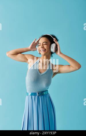 Eine Frau in einem blauen Kleid tanzt und lächelt, während sie Musik mit Kopfhörern hört. Stockfoto