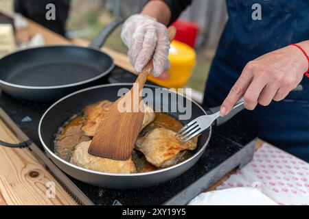Ein Koch kocht Fisch in einer Pfanne, mit einem Spachtel und einer Gabel, um den Fisch herum zu bewegen. Stockfoto