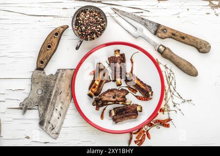 Schweinerippchen auf weißem Teller und Kräuter auf weißem hölzernem Hintergrund mit aufgerissener Farbe. Draufsicht. Stockfoto