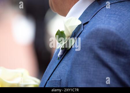Der Bräutigam trägt einen blauen Anzug mit einem weißen Rosenboutonniere am Revers und bereitet sich auf seine Hochzeitszeremonie vor Stockfoto