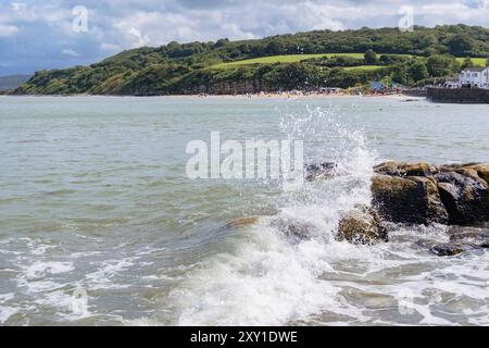 Wellen plätschern auf Felsen im Vordergrund mit Blick über die Benllech Bay zum Strand. Benllech, Isle of Anglesey, Wales, Großbritannien Stockfoto