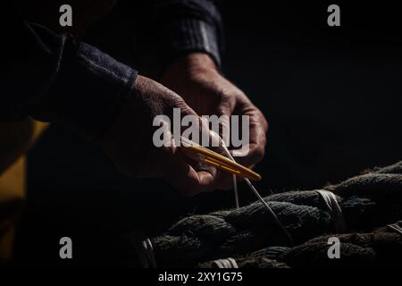 Die Hände eines Fischers, der Fischernetze mit Nadel und Faden repariert. Stockfoto