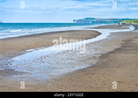 Sandkräuseln und Pools, die von der Flut am Marske Beach in North Yorkshire hinterlassen werden, mit Saltburn Town und den angrenzenden Klippen in der Ferne. Stockfoto