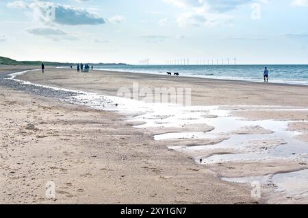 Sand, Steine und Schindelmuster und Wasserbecken, die von der rückläufigen Flut auf Marske am Sea Beach hinterlassen werden, mit sichtbarer Redcar Wind Farm am Horizont. Stockfoto