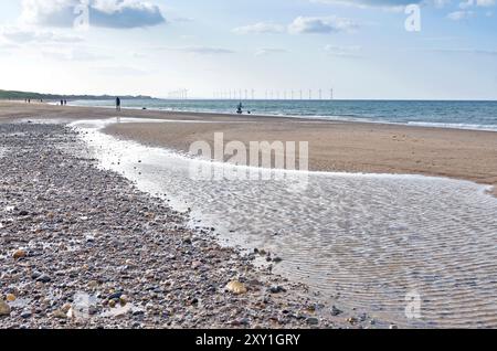 Sand, Steine und Schindelmuster und Wasserbecken, die von der rückläufigen Flut auf Marske am Sea Beach hinterlassen werden, mit sichtbarer Redcar Wind Farm am Horizont. Stockfoto