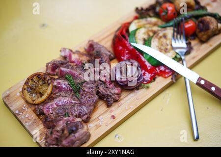 In Scheiben geschnittenes, seltenes Steak mit gegrilltem Gemüse auf einem Holzbrett. Stockfoto
