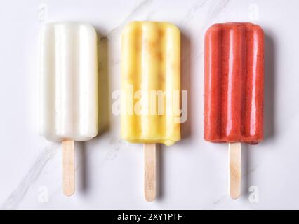 Draufsicht der drei verschiedenen Eis am Stiel auf einem Marmor Zähler nach oben. Roten, gelbe und weiße Früchten aromatisiert Pops. Stockfoto