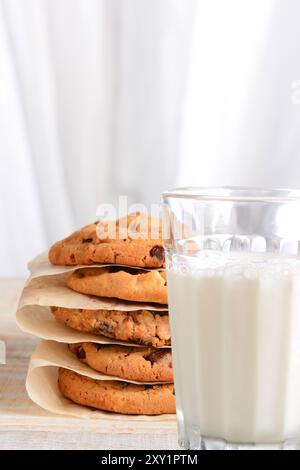 Nahaufnahme eines Stapels frisch gebackener Schokoladenkekse und eines Glases Milch. Vertikales Format mit unscharfem Hintergrund und Kopierbereich. Stockfoto