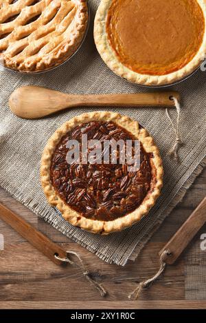 Vertikale Hochwinkelansicht von drei Torten für Ein Thanksgiving-fest. Pekan vorne mit Apfel- und Kürbiskuchen im Hintergrund. Auf Sackleinen mit Holz Stockfoto