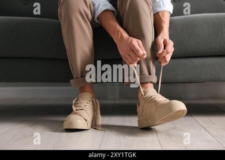 Mann, der drinnen einen Schnürsenkel auf dem Sofa bindet, Nahaufnahme Stockfoto