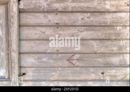 Eine verwitterte Holzwand mit einem schwachen roten Pfeil, der die Richtung anzeigt und Alter und Geschichte anzeigt. Stockfoto