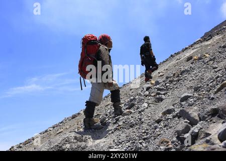 Zwei Bergsteiger nehmen sich auf dem Weg zum Gipfel des Mount Merapi Zeit auf einem Stück Sand und Felsen. Stockfoto