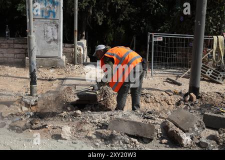 Palästinensisch-arabische ausländische Arbeiter, die eine Schutzweste tragen, verwenden eine Schaufel oder einen Spaten, um Erde, Beton und Steine zu bewegen, um einen Bürgersteig vorzubereiten, der umgebaut werden soll Stockfoto