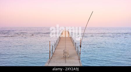 Foto eines leeren Stuhls auf einem hölzernen Pier bei einem violetten Sonnenuntergang. Stockfoto