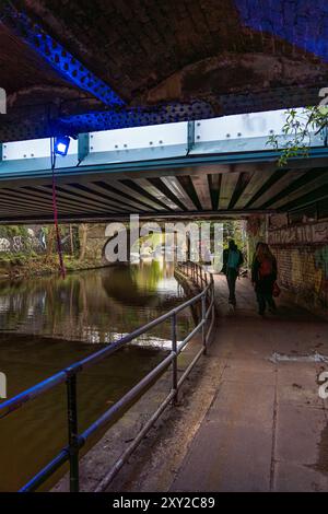 Freunde spazieren unter einer Brücke der Regent's Canal Promenade mit Hausbooten und Graffiti an den Wänden. Stockfoto