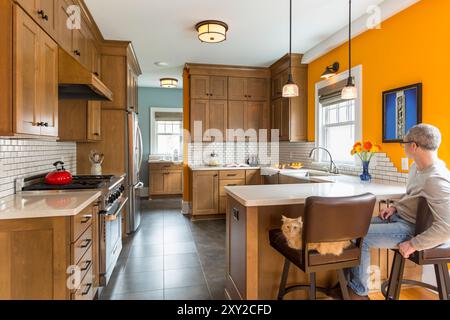 Renovierte Küche in einem älteren Haus mit Holzschränken und hellorangefarbenen Wänden und Mann und Katze sitzen auf Barhockern Stockfoto