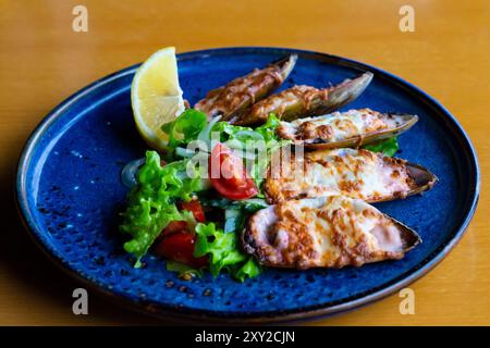 Fisch Und Meeresfrüchte. Muschelmuscheln. Gebackene Muscheln mit Käse, Koriander und Zitrone in Schalen auf gusseiserner schwarzer Platte. Teller mit Muscheln, kaltem Weißwein, Zitrone Stockfoto