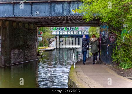 Zwei Freunde, Mann und Frau, die unter einer Brücke auf der Regent's Canal Promenade im Wohnviertel Maida Vale, London, laufen, mit Graffiti auf t Stockfoto