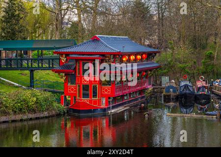 Großes rotes Boot, das in ein schwimmendes chinesisches Restaurant im Londoner Wohnviertel Regents Park von Maida Vale umgewandelt wurde, mit schmalen Booten, die auf dem angedockt sind Stockfoto