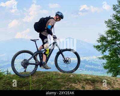 Radfahrer, der draußen mit dem E-Mountainbike fährt. Männliche Touristen, die auf einem grasbewachsenen Weg in den Bergen fahren, Helm und Rucksack tragen. Konzept von Sport, aktiver Freizeit und Natur. Stockfoto
