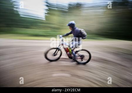 Bewegungsunschärfe. Radfahrer, der draußen mit dem E-Mountainbike fährt. Männliche Touristen fahren auf dem Weg im Wald. Konzept von Sport, aktiver Freizeit und Natur. Stockfoto