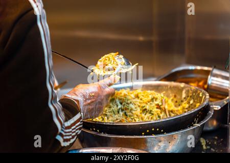 Chinesischer Koch mit Schürze und Kunststoffhandschuhen kocht mit Zutaten in einer Schüssel, um in der Küche eines chinesischen und asiatischen stal zum Mitnehmen Knödel zu machen Stockfoto