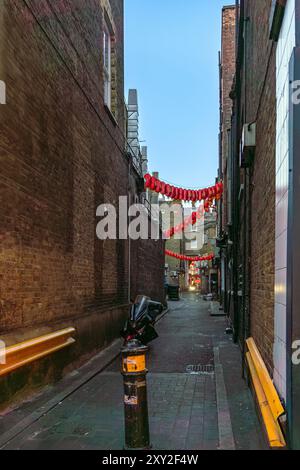 Dunkle, schmale Gasse in Chinatown mit Restaurantcontainern und roten chinesischen Laternen, die zwischen den Wänden hängen und einem Motorrad geparkt und einem anderen ap Stockfoto