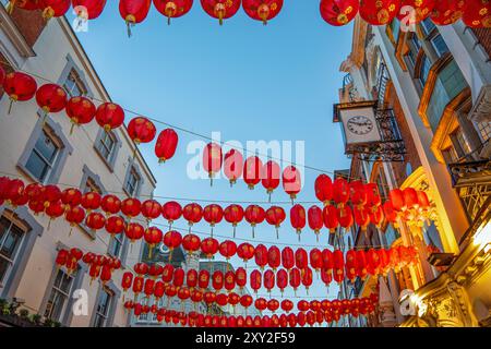 Blick auf den Sonnenuntergang von roten chinesischen Papierlaternen, die an den Fassaden einer Straße in Londons Chinatown in Soho hängen, unter einem klaren blauen Dämmerhimmel und einem typischen Stil Stockfoto