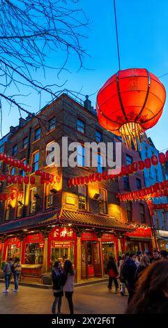 Touristen schlendern und plaudern an einer Straßenecke in Soho's Chinatown vor einem chio Restaurant und roten chinesischen Laternen, die an den Wänden hängen Stockfoto