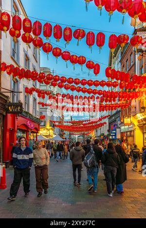 Fußgänger und Touristen schlendern entlang einer Straße in Chinatown in Soho und rote chinesische Laternen oder Papierlaternen hängen zwischen den Wänden. Stockfoto