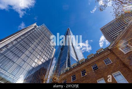 Flacher Blick auf den modernen pyramidenförmigen Glashochhaus The Shard mit blauem Himmel und einigen Wolken, die sich in den Fenstern der Gebäude spiegeln. Lo Stockfoto