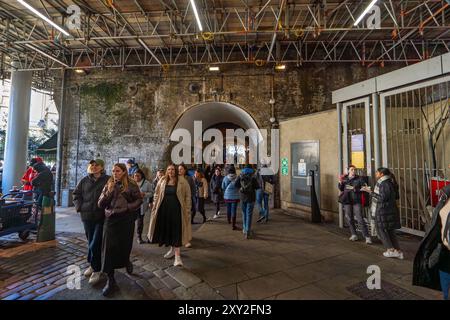 Eingang unter der Eisenbahnbrücke zum modernen Borough Market, wo Touristen schlendern und auf der Straße essen. Stockfoto