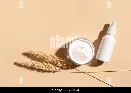Set von Kosmetikprodukten reichhaltige Gesichtscreme und Serum mit natürlichem trockenem Gras auf hellbeigem Hintergrund, Draufsicht, Kopierraum. Organisches natürliches Kollagen Stockfoto