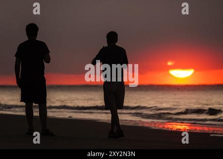 Isle Of Palms, Usa. August 2024. Am 27. August 2024 in Isle of Palms, South Carolina, laufen zwei Männer entlang des Strandes, während die Sonne einen schweren Nebel über dem Atlantischen Ozean durchbricht. Quelle: Richard Ellis/Richard Ellis/Alamy Live News Stockfoto