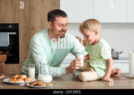 Glücklicher kleiner Junge und sein Vater mit verschiedenen Gebäckstücken, der Milch in der Küche trinkt Stockfoto