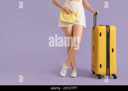 Junge Frau mit Koffer und Handtasche auf Fliederhintergrund Stockfoto